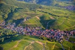 Aerial view of an Alsace wine village ringed by vineyards in the foothills of the Vosges at golden hour.