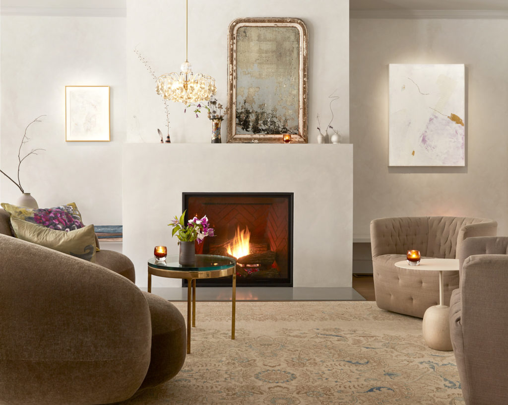 The Neverstill Wines tasting room lounge with a lit fireplace, curved mohair sofa, and antique mirror, designed by Amy Ilias. Photograph by Theo Coulombe.