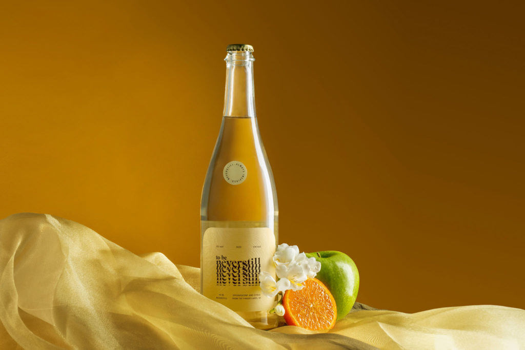 Neverstill Petnat from the Finger Lakes, styled with green apple, orange, and freesia. Photograph by Meghan Spiro.