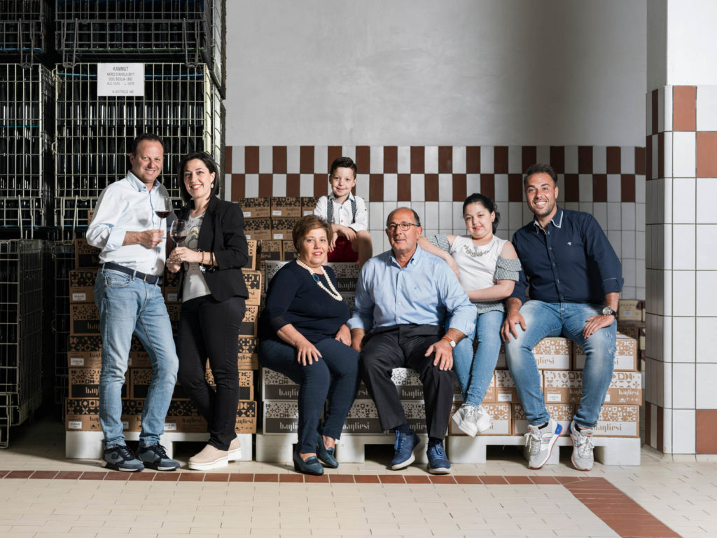 The Bagliesi family, three generations together, seated among stacked wine cases in their Sicilian cellar.